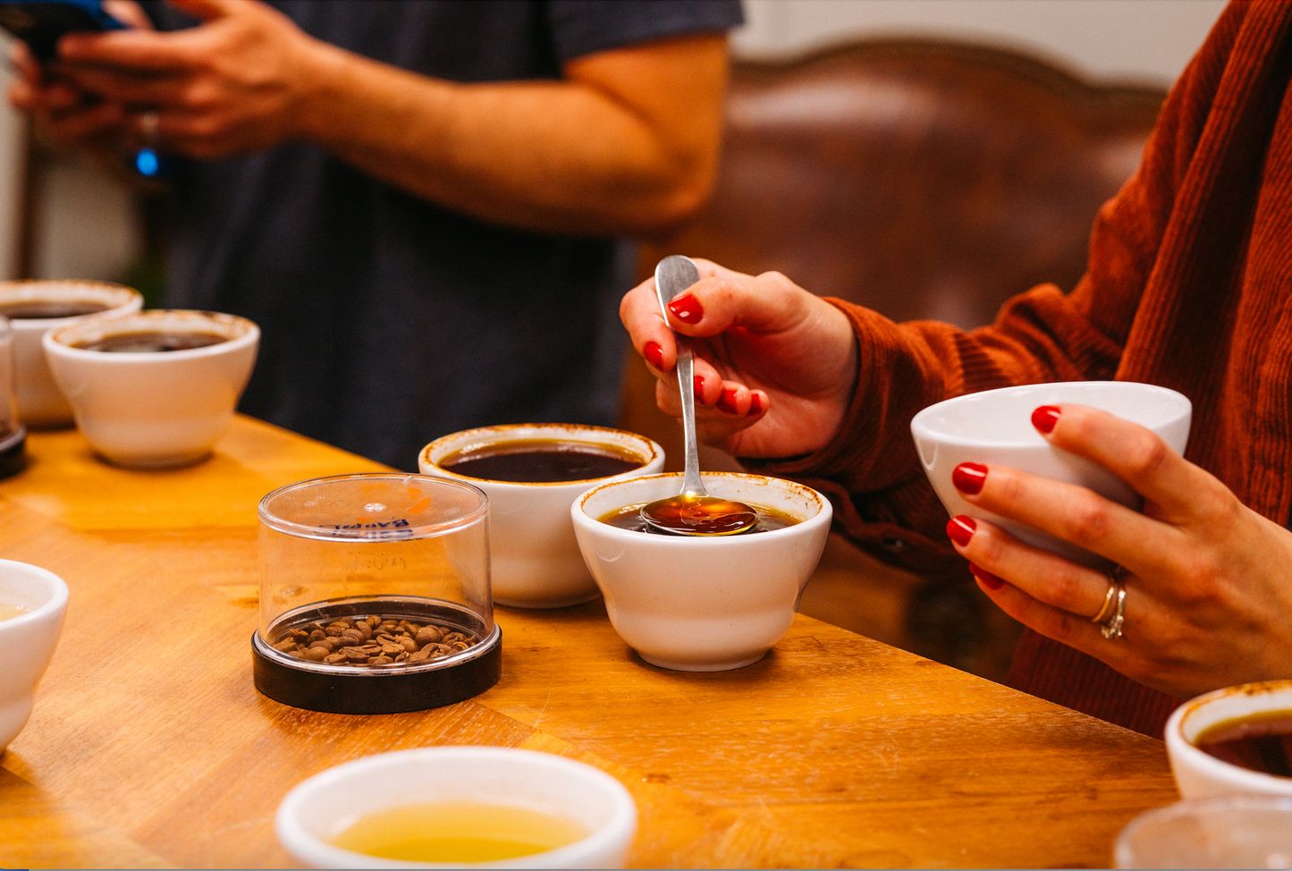 image of woman's hands holding cupping bowl and cupping spoon - dipping spoon into cupping bowl full of brewed coffee