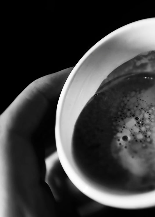 A black and white photo of fresh coffee brewed into a coffee cup