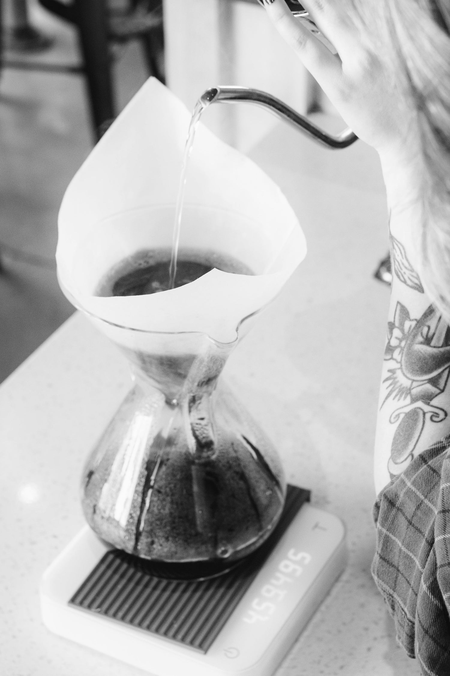 Black and white photo of a kettle pouring water into a chemex Brewer 