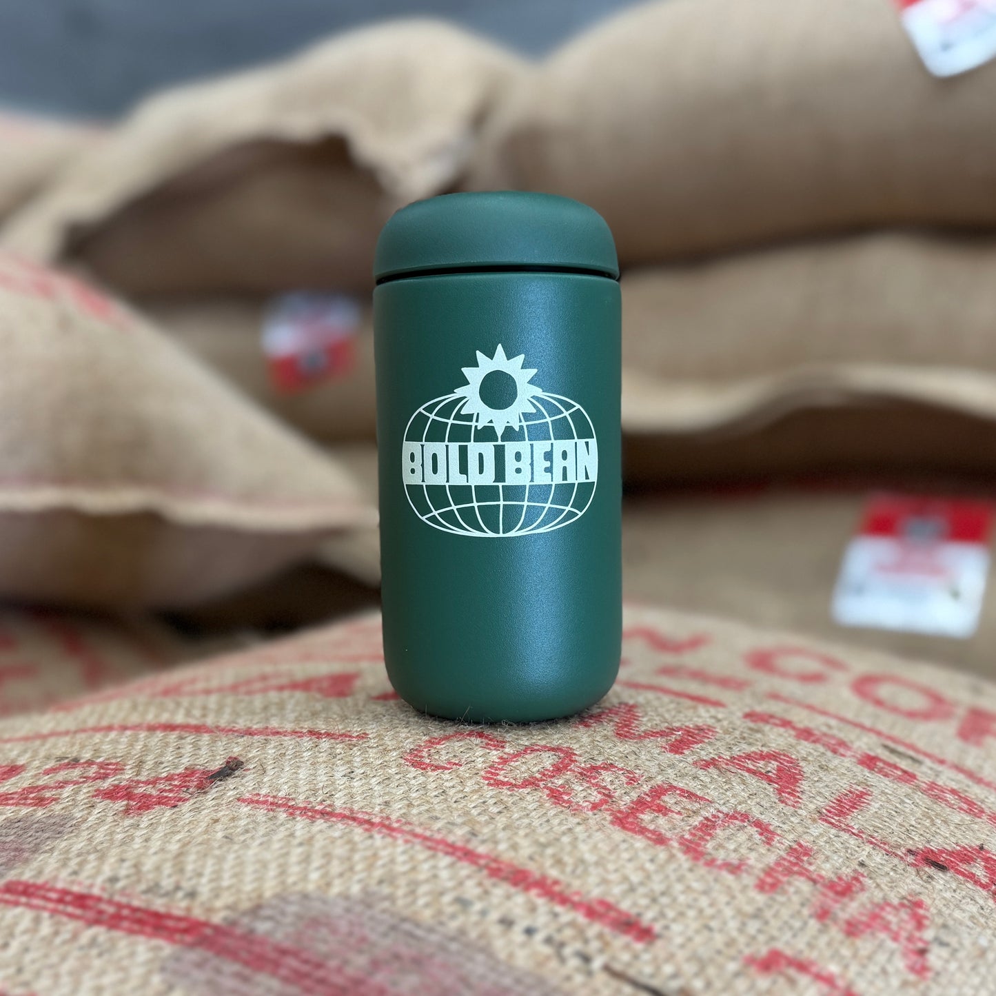 Green thermos with a logo on a burlap background