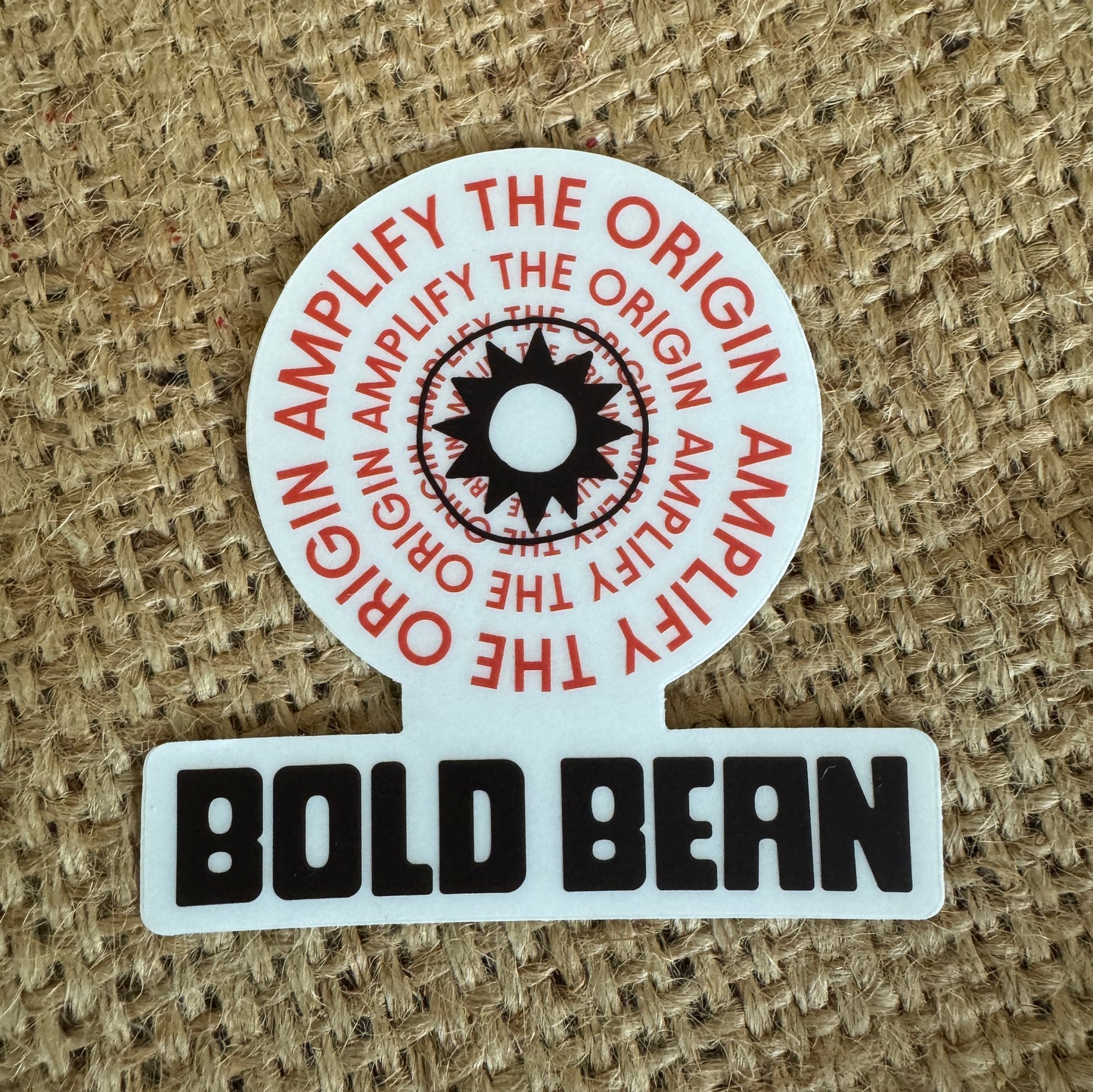 Round sticker with 'Amplify the Origin' text and 'Bold Bean' branding on a textured background