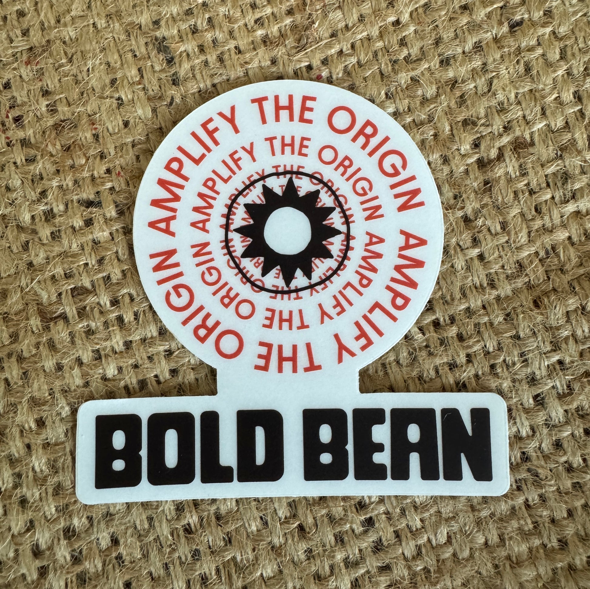 Round sticker with 'Amplify the Origin' text and 'Bold Bean' branding on a textured background