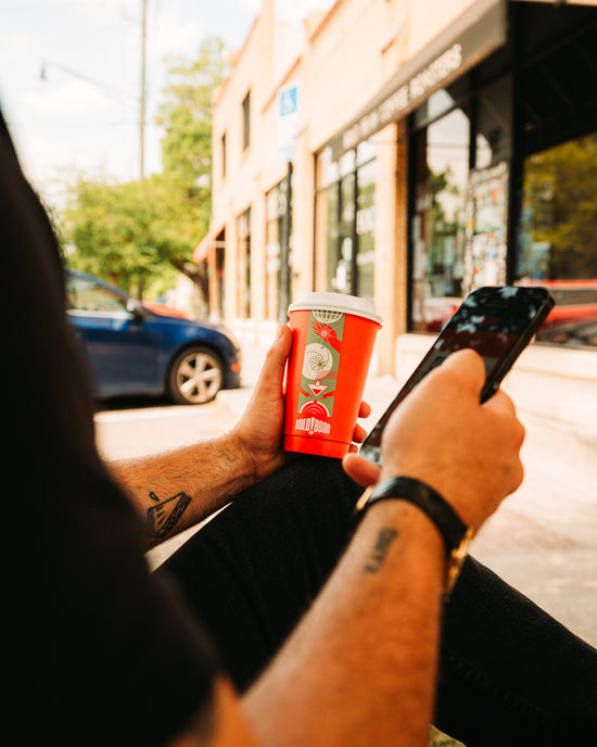 point of view image of person holding branded coffee cup in left hand and phone in right hand