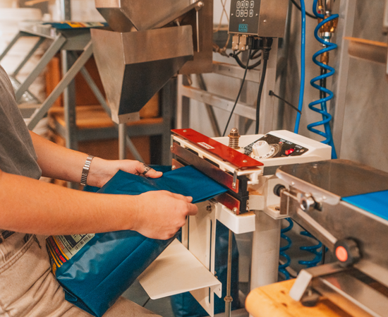 coffee bag being sealed with a sealer and other packaging equipment in background