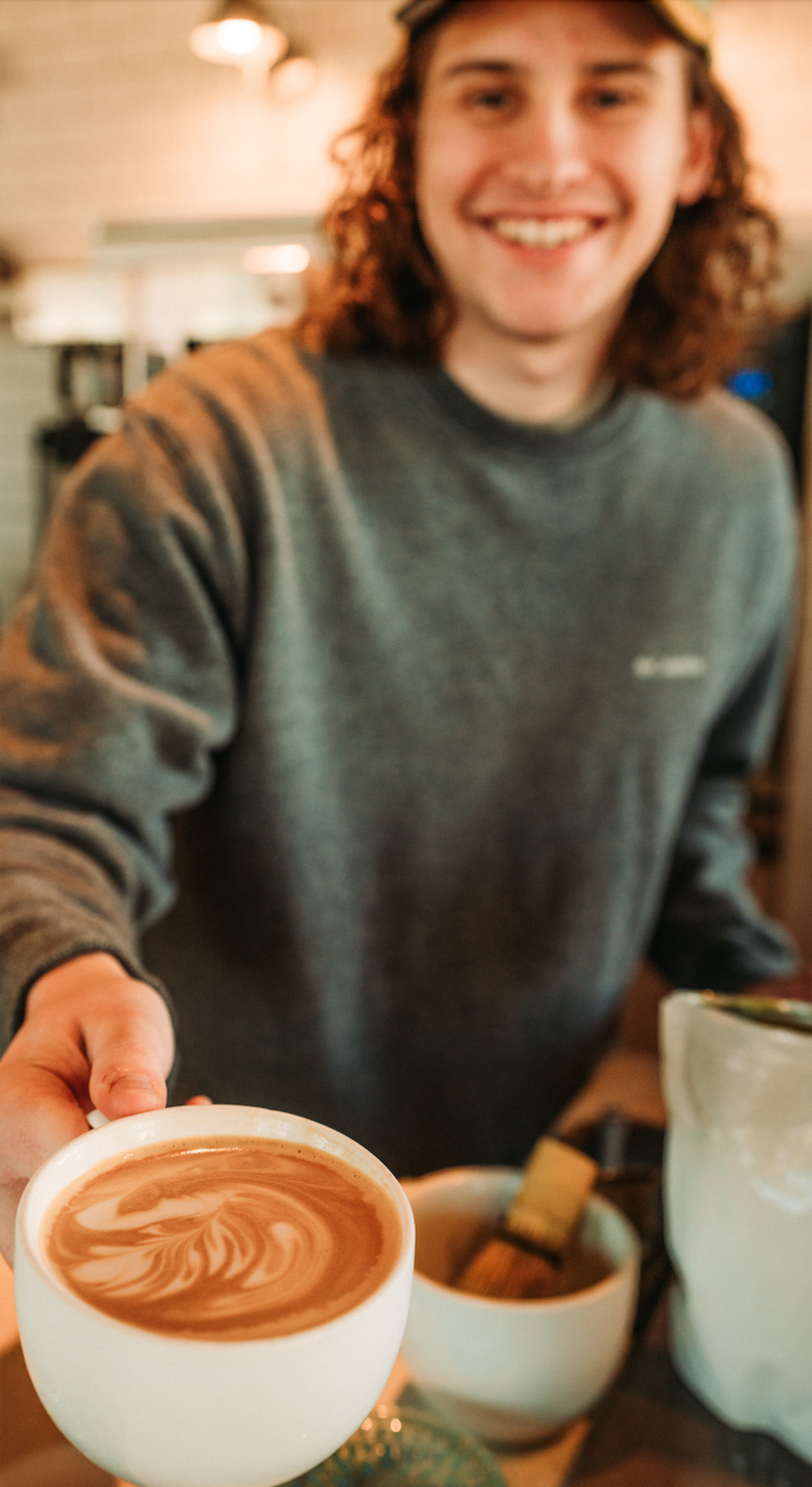 Person holding a cup of coffee with latte art in a coffee shop setting