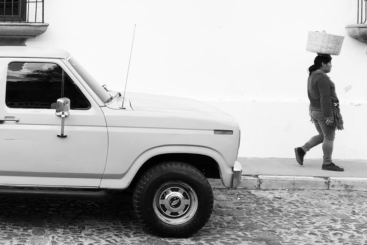 White truck parked on a cobblestone street with a person walking by in a black and white photo.